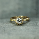 A yellow gold ring with a lab-grown diamond oceany bubble setting, resting on a textured gray surface.
