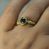 A close-up of a gold ring with a dark blue oval sapphire worn on a finger.