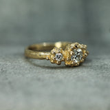 A gold ring with a textured, organic-shaped band with oceany bubble clusters of small and large lab-grown diamonds, resting on a gray textured surface.