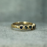 A gold ring with blue sapphires set in a textured, organic design, resting on a gray stone surface.