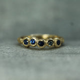 A gold ring with five small round dark blue gemstones set in a textured, organic cluster design, resting on a gray textured surface.