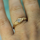 A close-up of a hand wearing a unique gold ring with a lab-grown  diamond and organic, branch-like sculpted details.