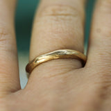 A close-up of a hand wearing a simple, water textured gold band ring.