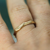 A close-up of a hand wearing a textured, wavy gold band ring.