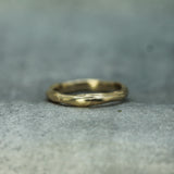 A textured, organic-shaped gold ring resting on a neutral gray stone-like surface.