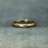 A textured, organic-shaped gold ring resting on a gray stone surface.