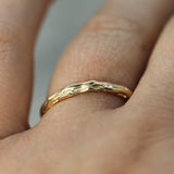 A close-up of a textured gold band ring worn on a finger.