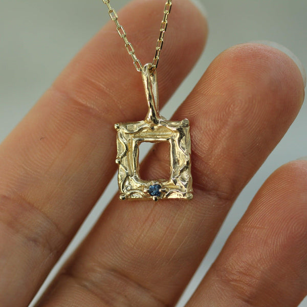 Gold pendant with a blue sapphire held between fingers against a neutral background
