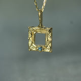 Gold pendant with a blue sapphire on a gray background