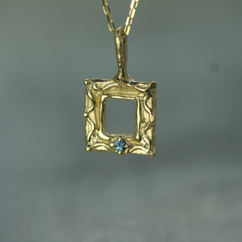 Gold pendant with a blue sapphire on a gray background