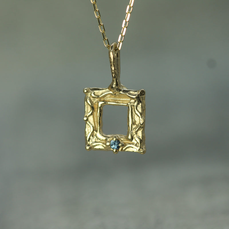 Gold pendant with a blue sapphire on a blurred background