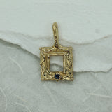 Gold frame pendant with a blue sapphire on a white surface 