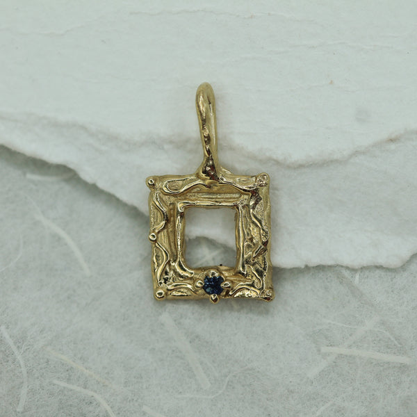 Gold frame pendant with a blue sapphire on a white surface 