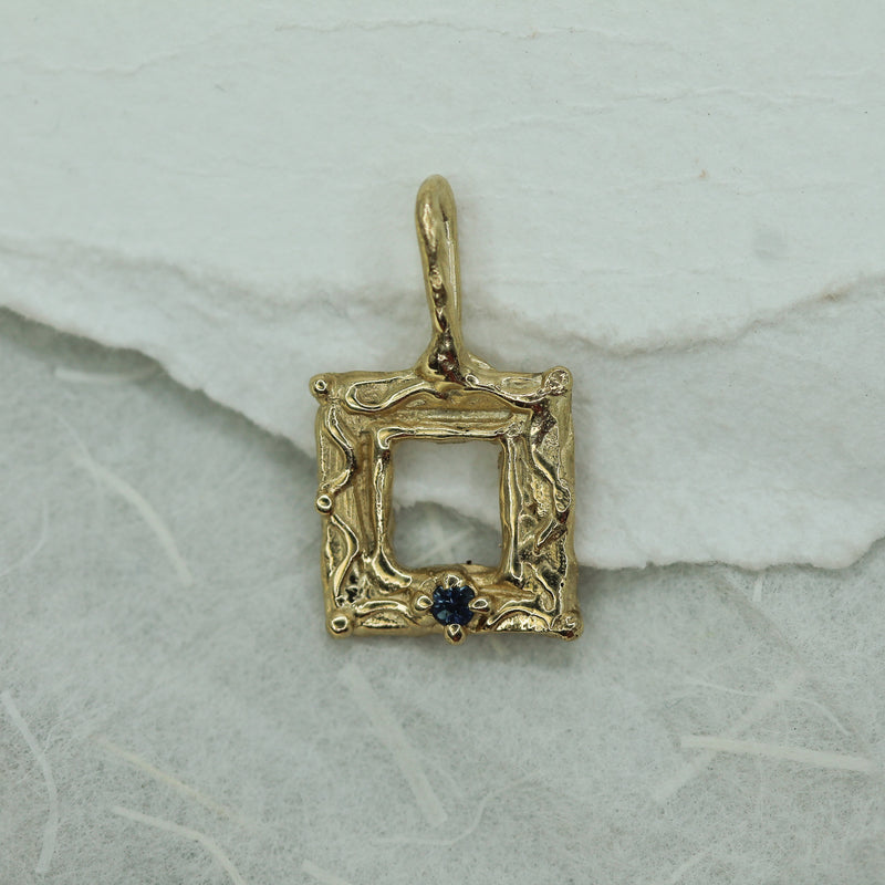 Gold frame pendant with a blue sapphire on a white surface 