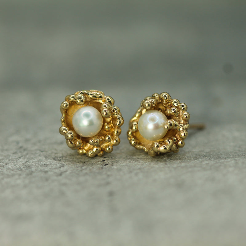 Gold earrings with pearl centers on a textured surface