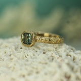 Gold ring with a teal sapphire showing a san-textured band