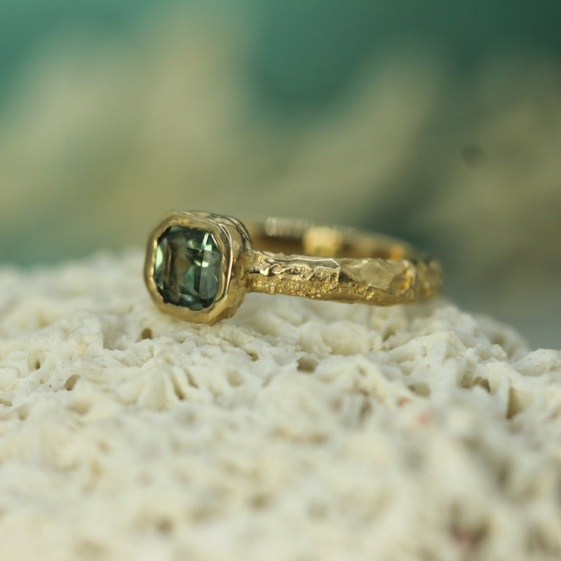 Gold ring with a teal sapphire showing a san-textured band