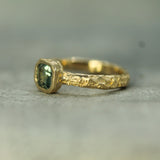 Gold ring with a teal sapphire on a gray background