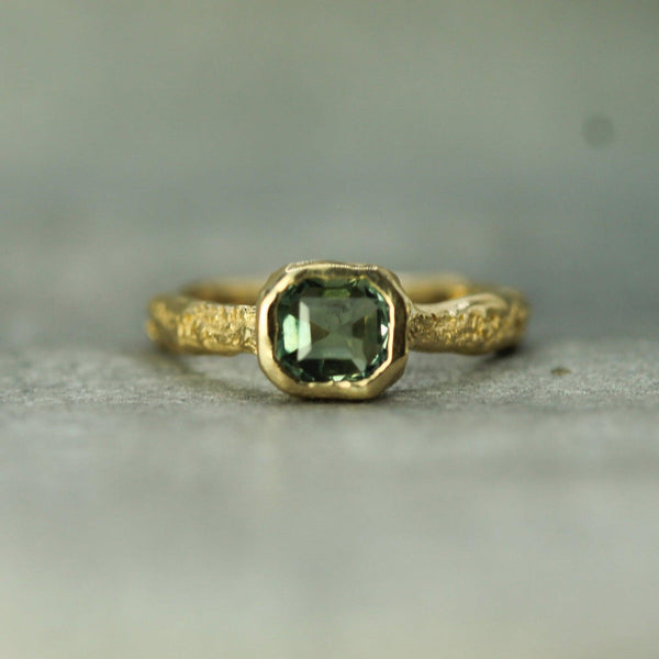 14k Gold ring with a teal sapphire on a blurred background