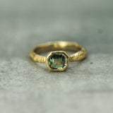 Gold ring with a teal sapphire on a textured surface
