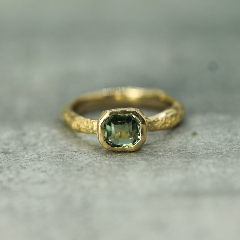 Gold ring with a teal sapphire on a textured surface