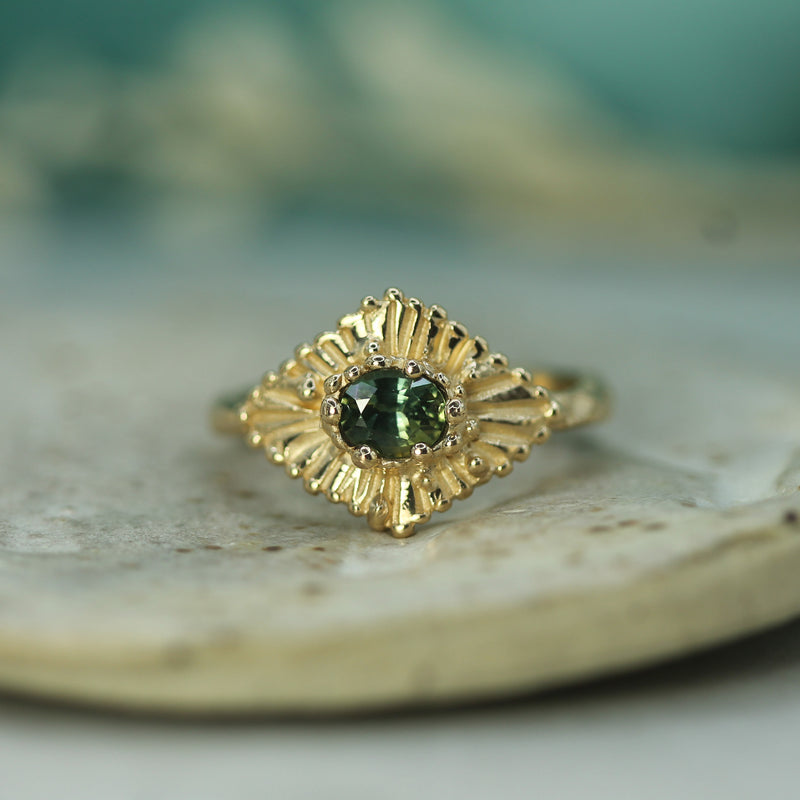 Gold ring with a teal sapphire on a textured surface