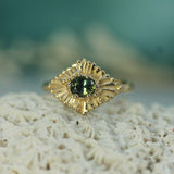 Gold ring with a teal sapphire on a textured surface