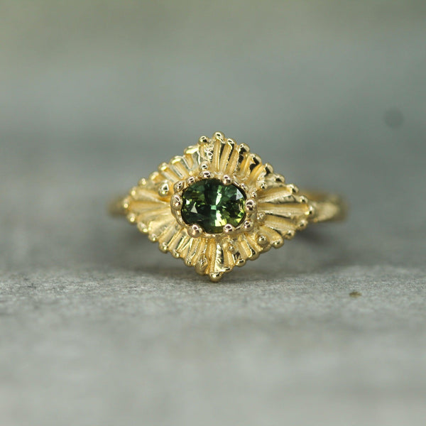 Gold ring with a teal sapphire  on a textured surface