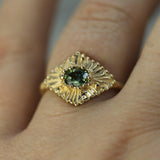 Gold ring with a teal sapphire  on a finger