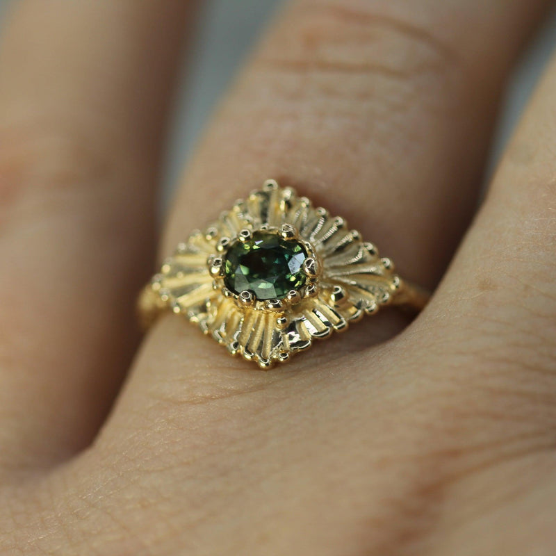 Gold ring with a teal sapphire  on a finger