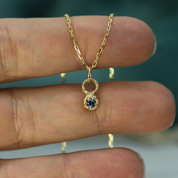 Gold necklace with a blue gemstone pendant held between fingers against a blurred background
