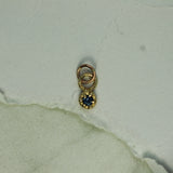 Gold charm with a blue gemstone on a textured light green background