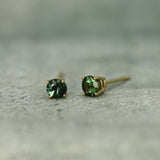 Pair of teal sapphire stud earrings on a textured surface
