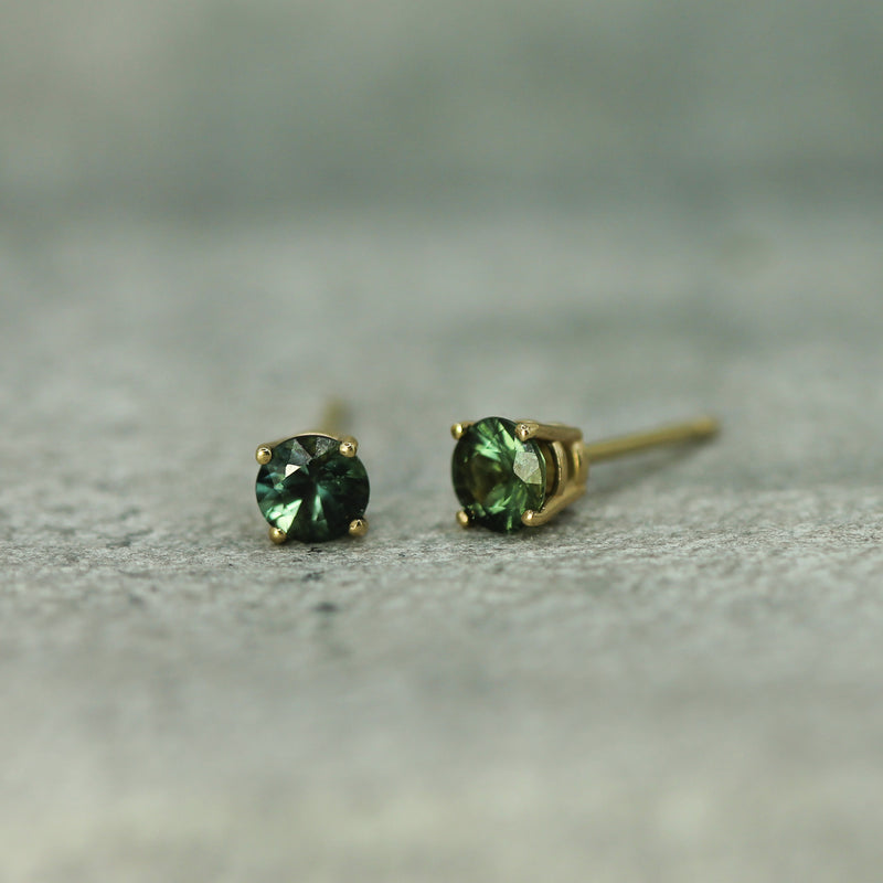 Pair of teal sapphire stud earrings on a textured surface