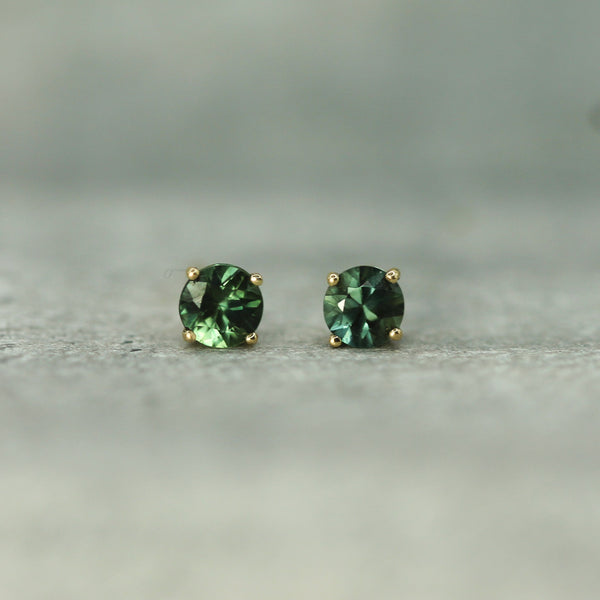 Pair of teal sapphire stud earrings on a neutral background