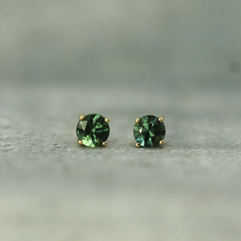 Pair of teal sapphire stud earrings on a neutral background