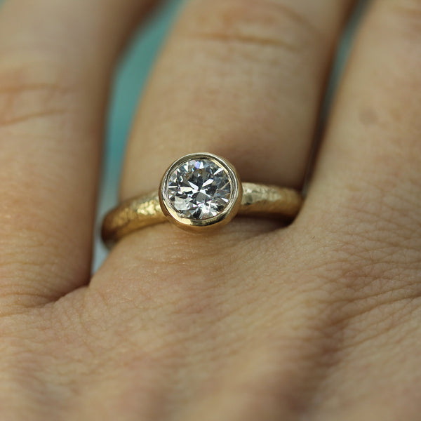 14k Yellow gold ring with a diamond on a person's finger against a light blue background