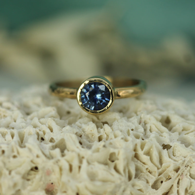Gold ring with a blue sapphire on a textured surface