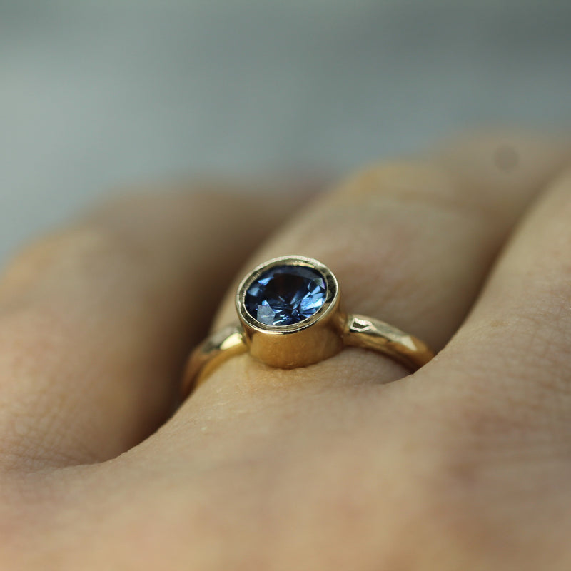 Gold ring with a blue sapphire on a finger against a blurred background