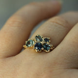 Gold ring with blue sapphires on a finger against a neutral background