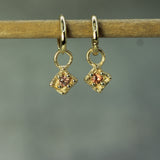 Gold earrings with orange sapphires on a wooden stick against a gray background