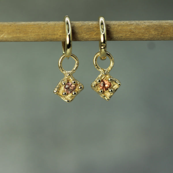 Gold earrings with orange sapphires on a wooden stick against a gray background