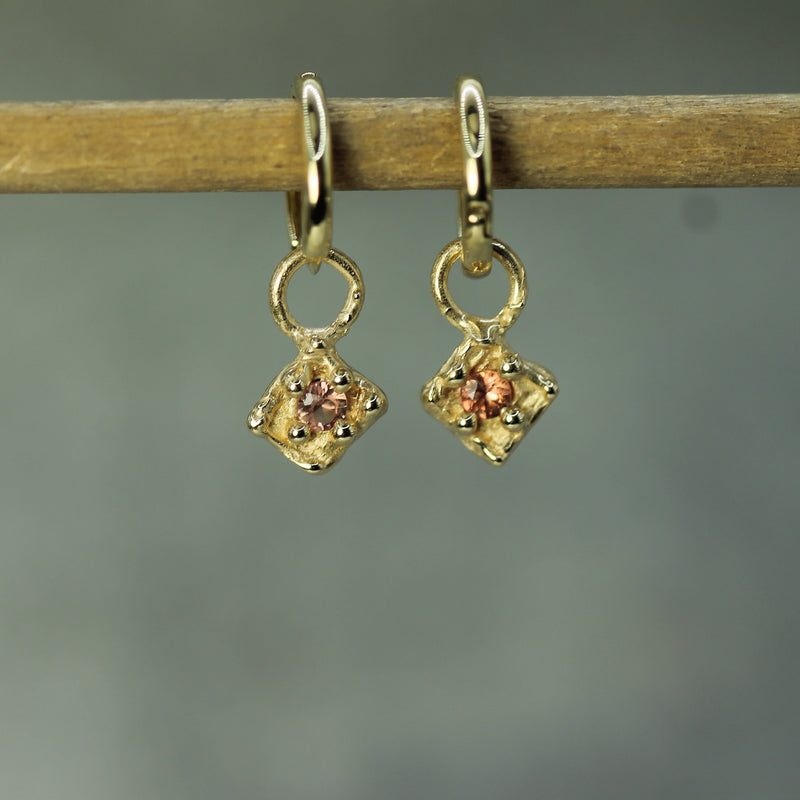 Gold earrings with orange sapphires on a wooden stick against a gray background