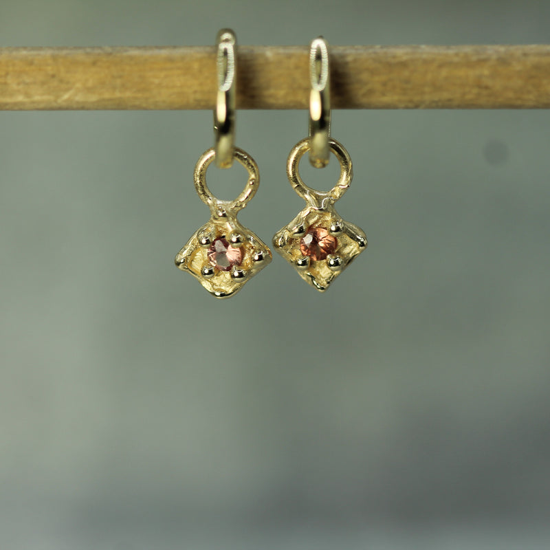 Gold earrings with sapphries on a wooden stick against a blurred background