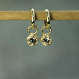 Gold earrings with circular designs on a wooden stick against a gray background