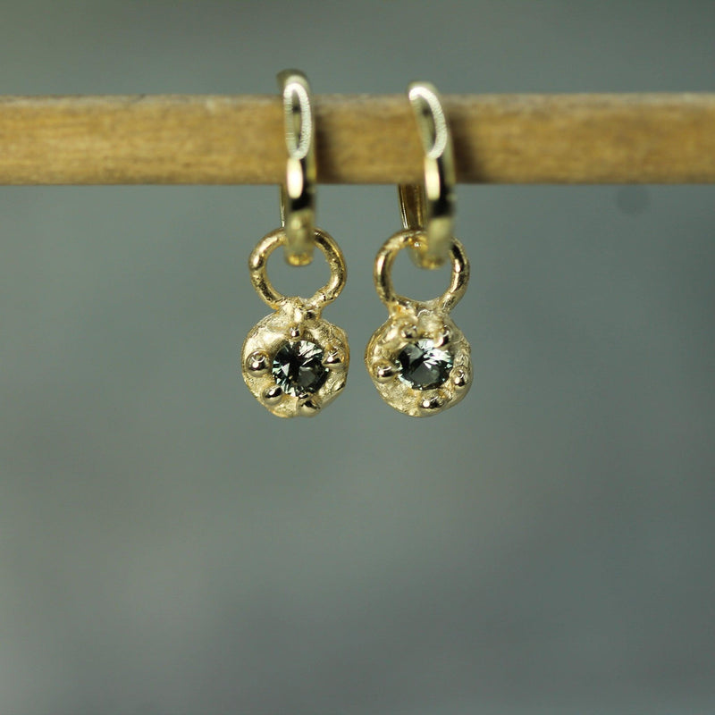 Gold earrings with circular designs on a wooden stick against a gray background