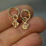 Gold hoop earrings with dangling charms held between fingers against a neutral background