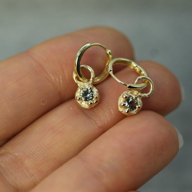 Gold earrings with sapphires held between fingers against a neutral background