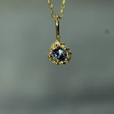 Gold pendant with a blue sapphire 
on a blurred gray background