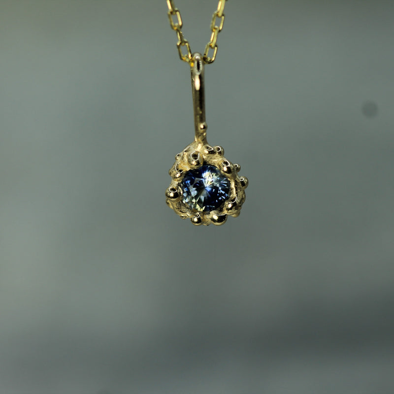 Gold pendant with a blue sapphire 
on a blurred gray background
